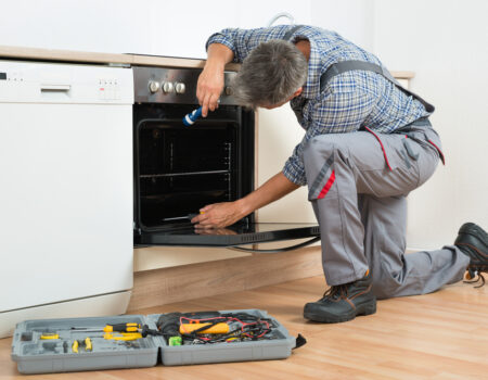 Full,Length,Of,Repairman,Examining,Oven,With,Flashlight,In,Kitchen